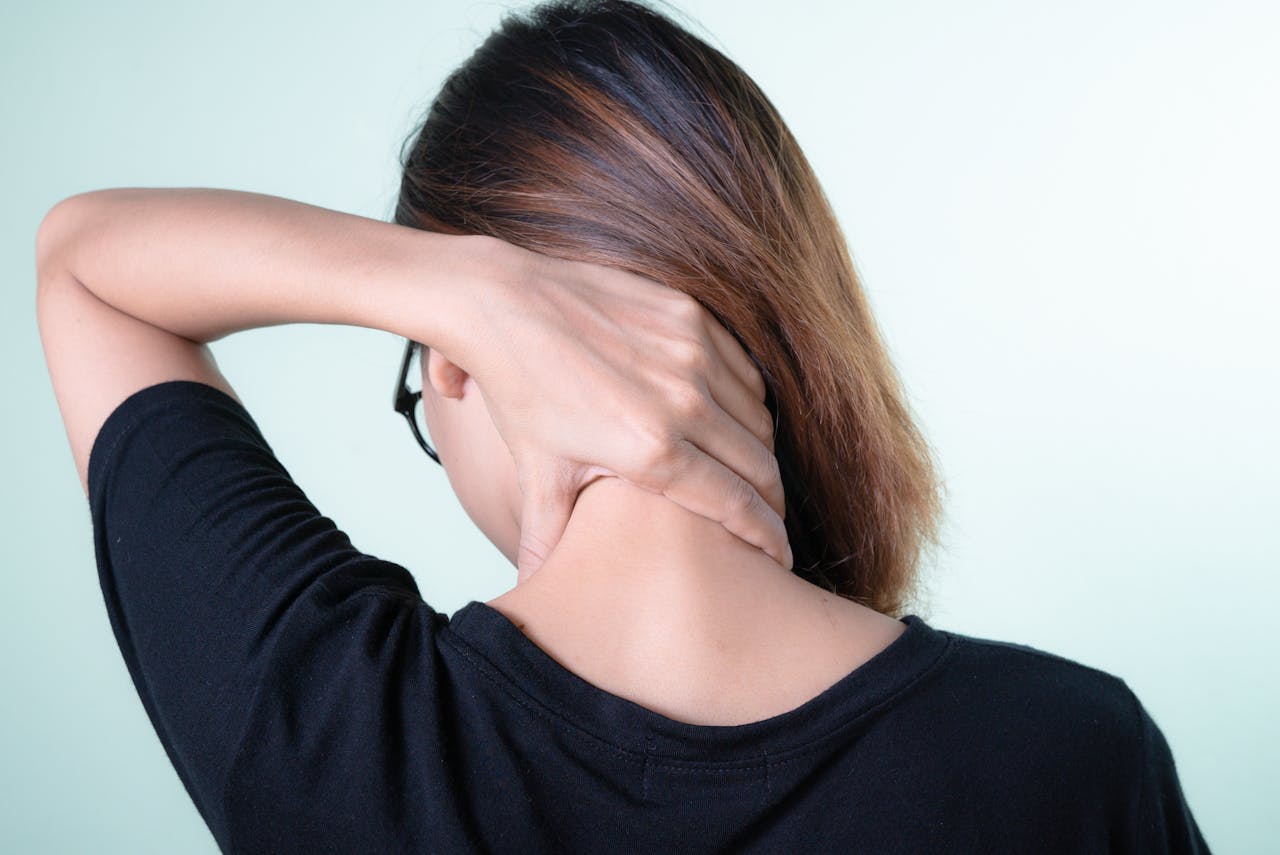 Mujer tocándose la parte trasera del cuello con una mano, reflejando incomodidad por dolor de cuello al dormir y buscando aliviarlo