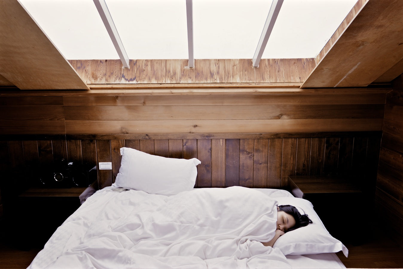 Mujer durmiendo en una habitación de madera iluminada por luz natural, simbolizando el descanso y el proceso de los sueños.